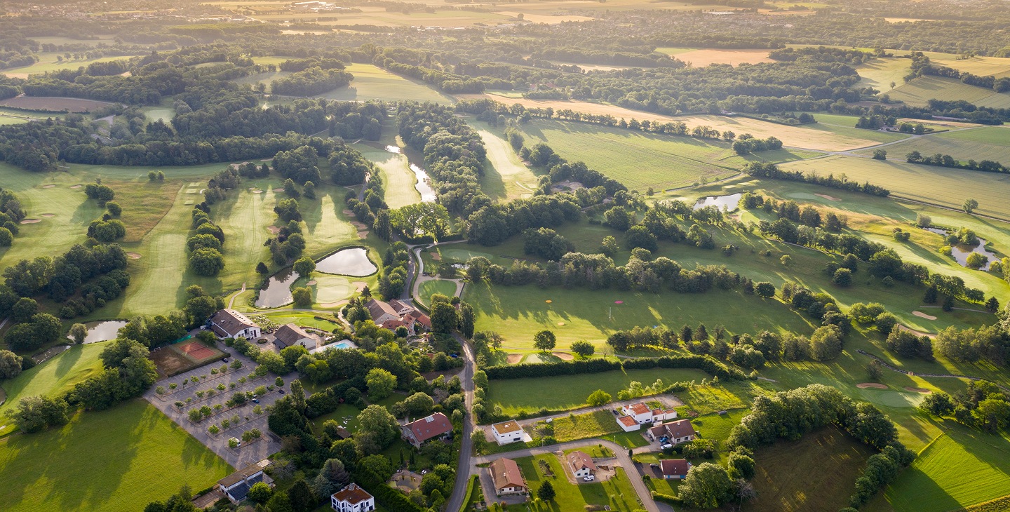 Vue aérienne d'un parcours de golf verdoyant au Pays de Gex, ensoleillé