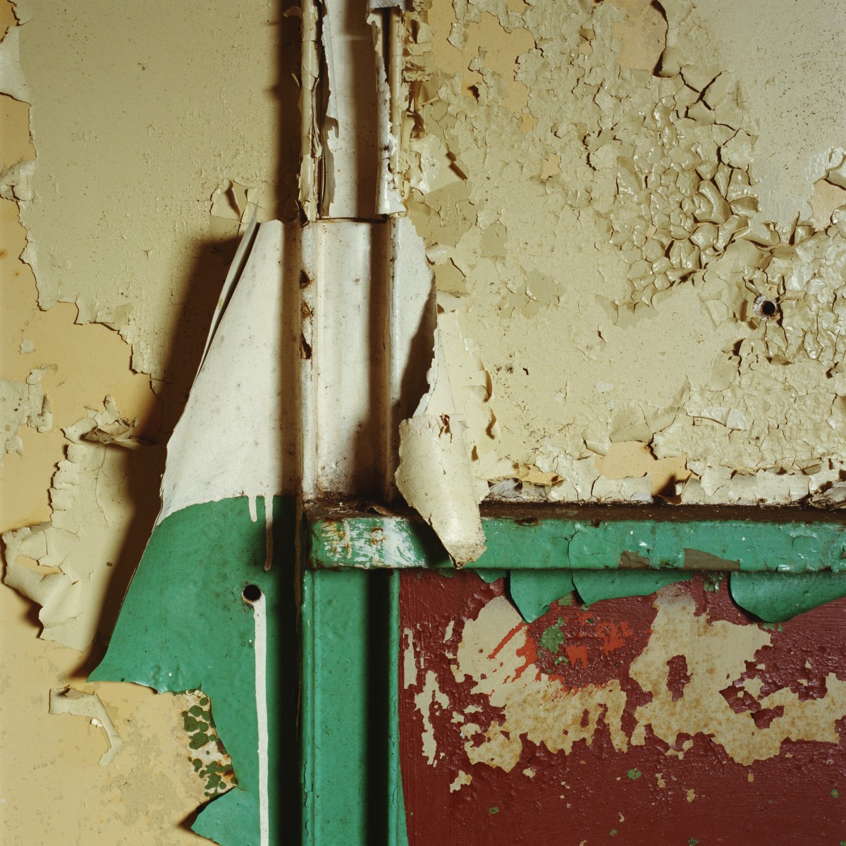 Mur avec peintures écaillées en couches vert, crème et rouge, risque plomb